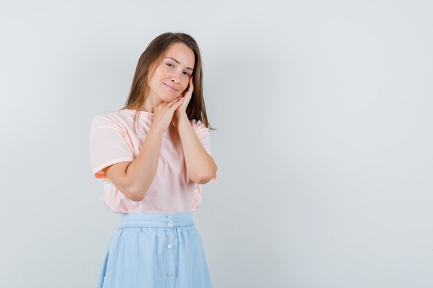 Jeune fille en t-shirt, jupe appuyée sur les paumes comme oreiller et à la jolie vue de face.