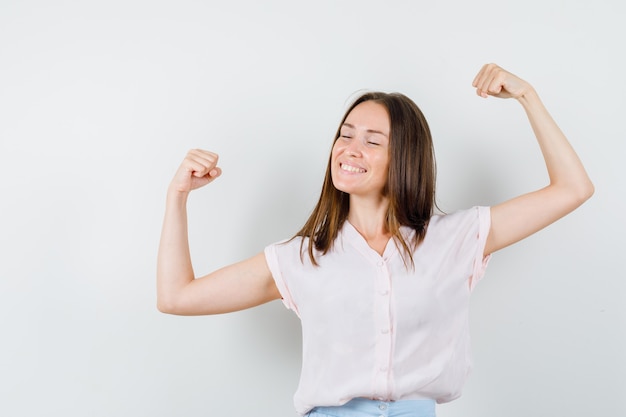 Jeune fille en t-shirt, jupe montrant le geste du gagnant et à la béatitude, vue de face.