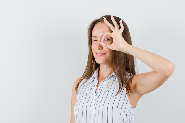 Jeune fille en t-shirt montrant un geste ok et un clin d'œil, vue de face.