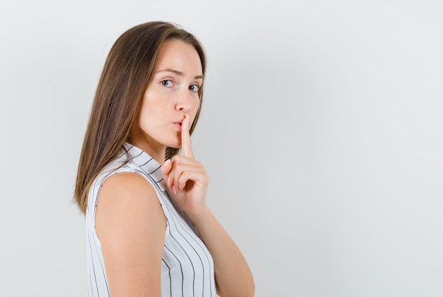 Jeune fille en t-shirt montrant le geste de silence et à la recherche sensible.