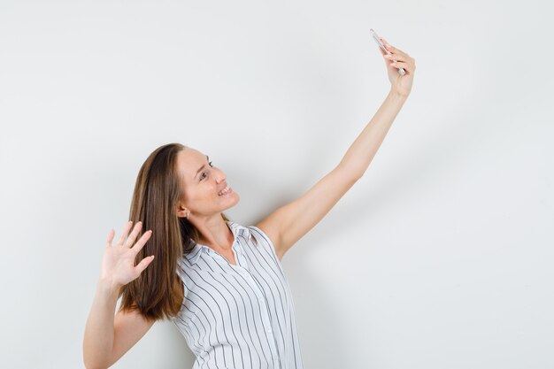 Jeune fille en t-shirt posant tout en prenant selfie et en regardant heureux, vue de face.