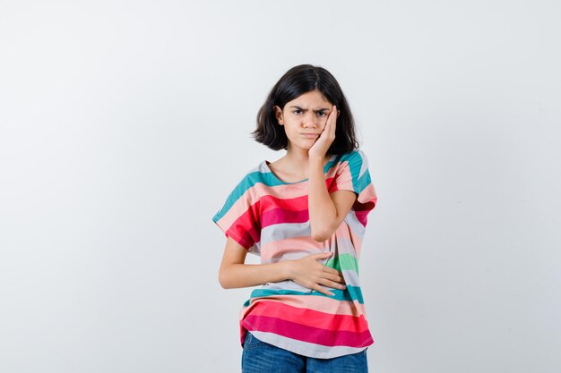 Jeune fille en t-shirt rayé coloré ayant mal aux dents et l'air ennuyé, vue de face.