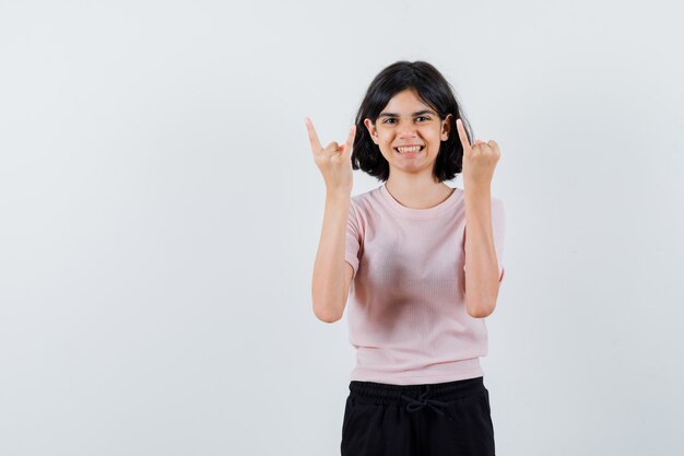 Jeune fille en t-shirt rose et pantalon noir montrant un geste de métal lourd et un petit doigt et à la joie