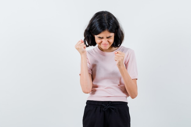 Jeune fille en t-shirt rose et pantalon noir montrant la pose du gagnant et l'air heureux