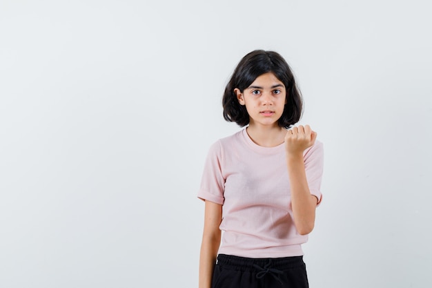 Jeune fille en t-shirt rose et pantalon noir serrant le poing et à la jolie