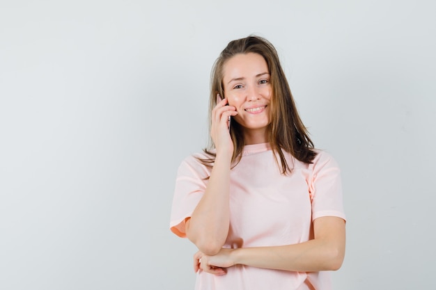 Jeune fille en t-shirt rose parlant au téléphone mobile et à la jolly, vue de face