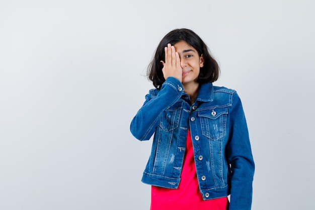 Jeune Fille En T-shirt Rouge Et Veste En Jean Couvrant Les Yeux Avec La Main Et L'air Heureux, Vue De Face.