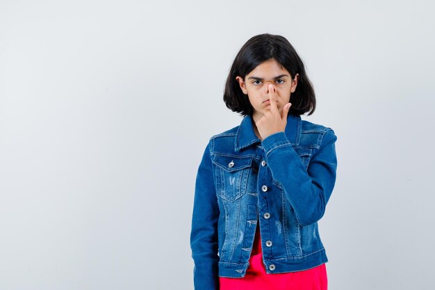 Jeune fille en t-shirt rouge et veste en jean mettant l'index sur la bouche et l'air sérieux, vue de face.