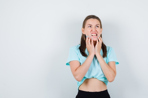 Jeune fille en t-shirt turquoise, pantalon avec les doigts sur le menton et à la recherche de ressentiment, vue de face.