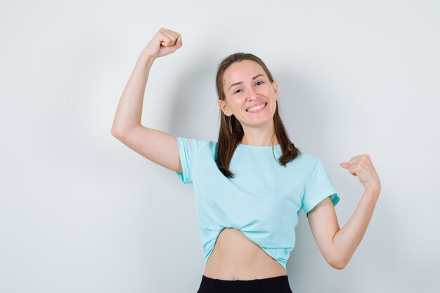 Photo gratuite jeune fille en t-shirt turquoise, pantalon montrant le geste du vainqueur et l'air joyeux, vue de face.