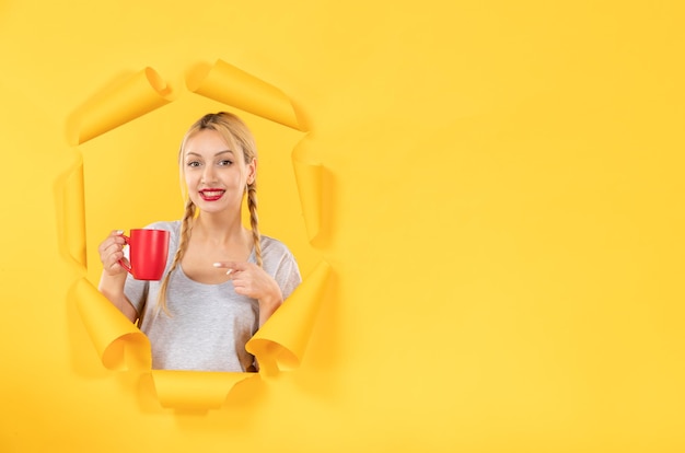 Jeune fille avec une tasse de thé sur fond de papier jaune déchiré shopping du visage