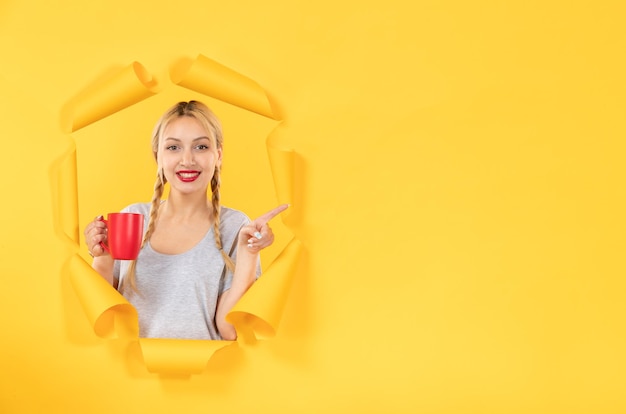 Jeune fille avec une tasse de thé sur une surface de papier jaune déchiré