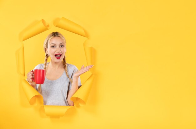 Jeune fille avec une tasse de thé sur une surface de papier jaune déchiré