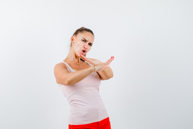 Photo gratuite jeune fille tenant deux bras croisés, ne faisant aucun signe en haut beige et pantalon rouge et à la confiance. vue de face.