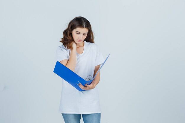 Jeune fille tenant la main sur le cou, regardant dans le dossier en t-shirt blanc et à la recherche de occupé. vue de face.