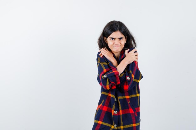 Jeune fille tenant les mains sur les épaules en chemise à carreaux et l'air épuisé, vue de face.