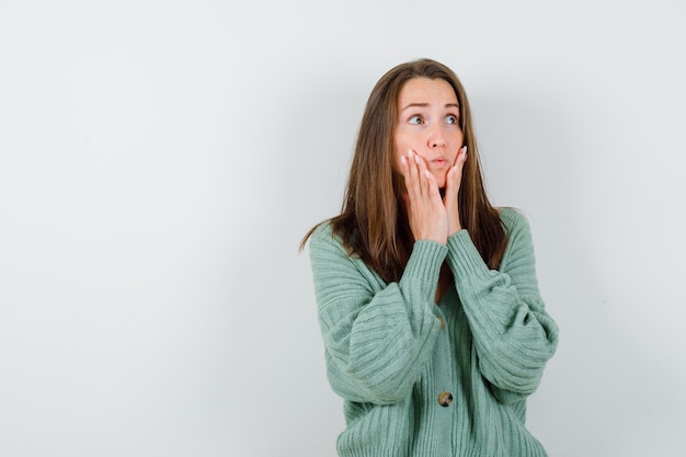 Jeune fille tenant les mains sur la mâchoire, regardant ailleurs en maille, jupe et à la vue excitée, de face.