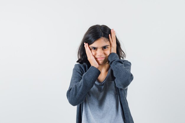 Jeune fille tenant les mains sur la tête en t-shirt gris clair et sweat à capuche zippé gris foncé et à l'ennui,