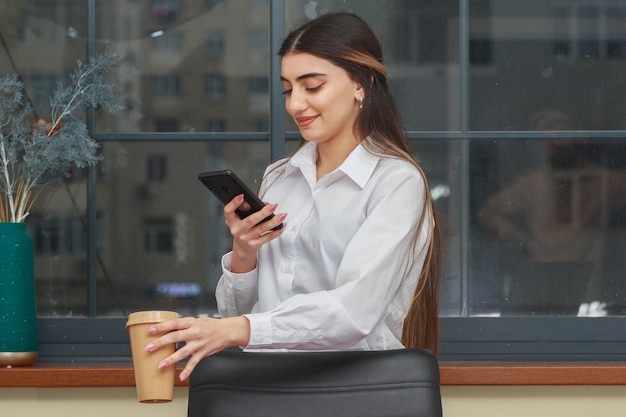 Jeune fille tenant une tasse de café et regardant le téléphone