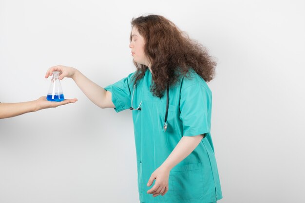 jeune fille en uniforme vert tenant un bocal en verre avec du liquide bleu.