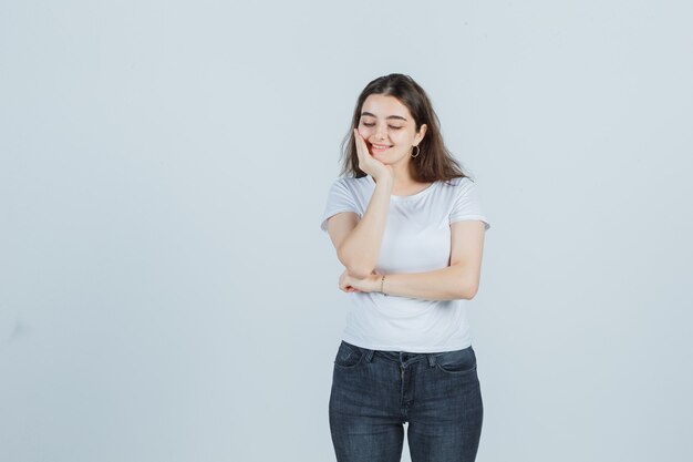 Jeune fille vérifiant la peau sur les tempes en t-shirt, jeans et à la joyeuse vue de face.