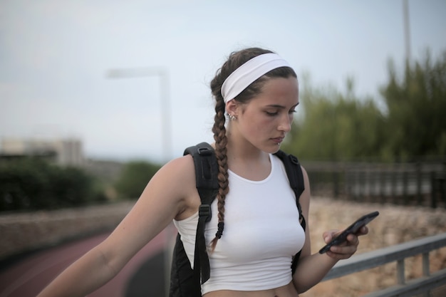 Photo gratuite jeune fille voyageuse avec des tresses et un sac à dos en regardant son téléphone