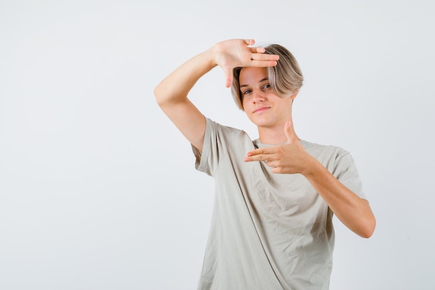 Jeune garçon adolescent faisant un geste de cadre par des pistolets à doigt en t-shirt et ayant l'air confiant. vue de face.