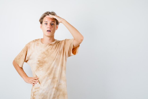 Jeune garçon adolescent gardant la main sur la tête en t-shirt et à se demander. vue de face.