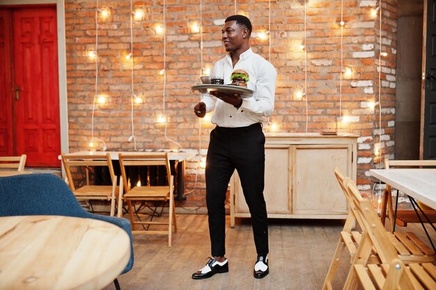 Un jeune garçon afro-américain tient un plateau avec un hamburger au restaurant