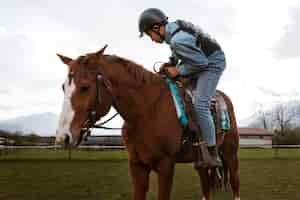 Photo gratuite jeune garçon apprenant à monter à cheval