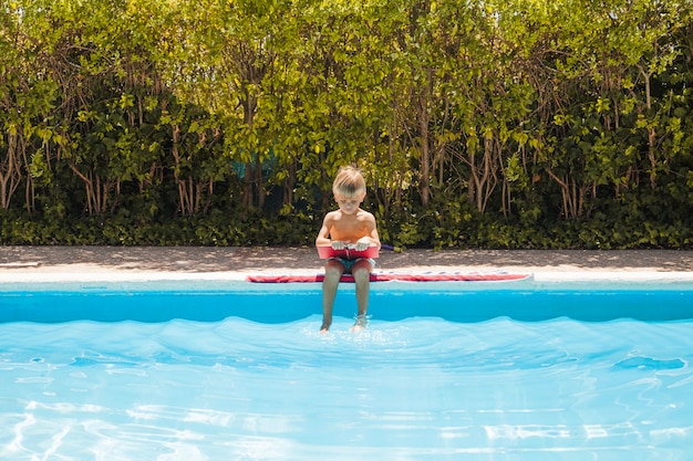 Jeune garçon assis en piscine avec un livre