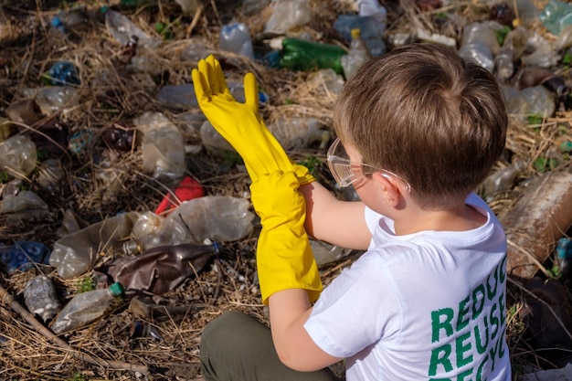 Jeune garçon caucasien blanc avec un symbole de recyclage sur son t-shirt et des lunettes mettant des gants jaunes