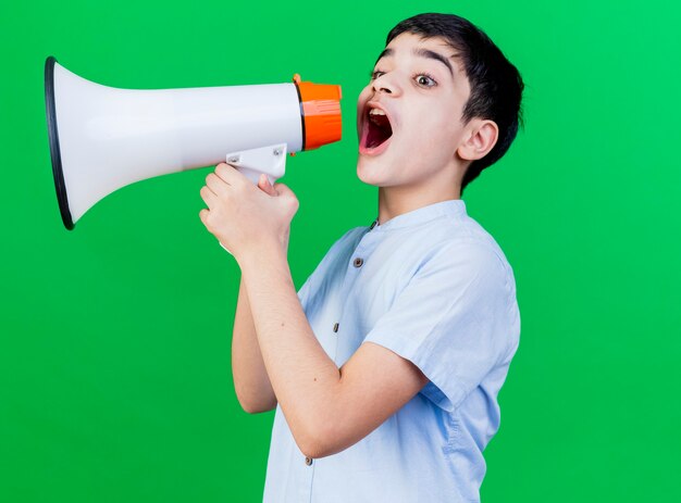 Jeune garçon caucasien debout en vue de profil parler par haut-parleur isolé sur fond vert avec espace de copie