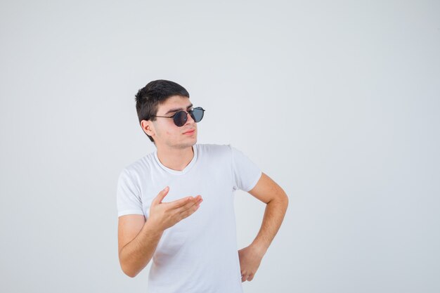 Jeune garçon faisant semblant de montrer quelque chose en t-shirt et à la confiance en soi, vue de face.