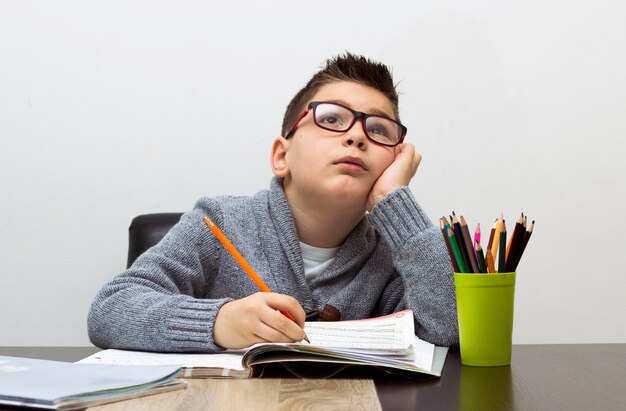 Jeune garçon frustré par les devoirs, écrit à la maison. Garçon étudiant à la table. Dessin d&#39;enfant avec un crayon.