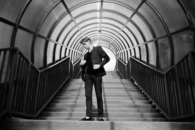 Photo gratuite jeune garçon macho élégant en veste noire posée à l'extérieur de la rue incroyable homme modèle au tonnel d'escalier rouge