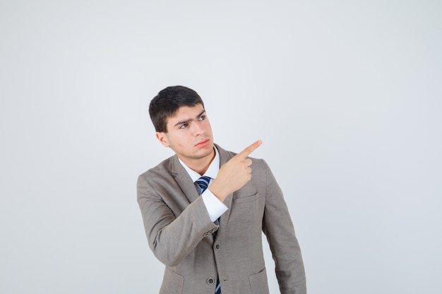 Jeune garçon pointant vers l'extérieur avec l'index en costume formel et à la recherche de sérieux. vue de face.