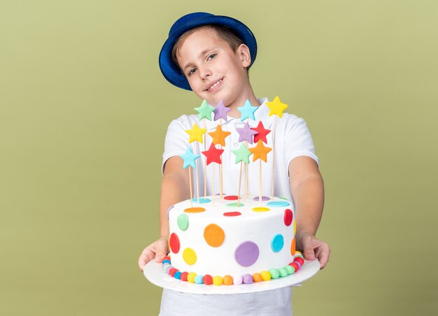 jeune garçon slave souriant avec un chapeau de fête bleu tenant un gâteau d'anniversaire isolé sur un mur vert olive avec espace pour copie