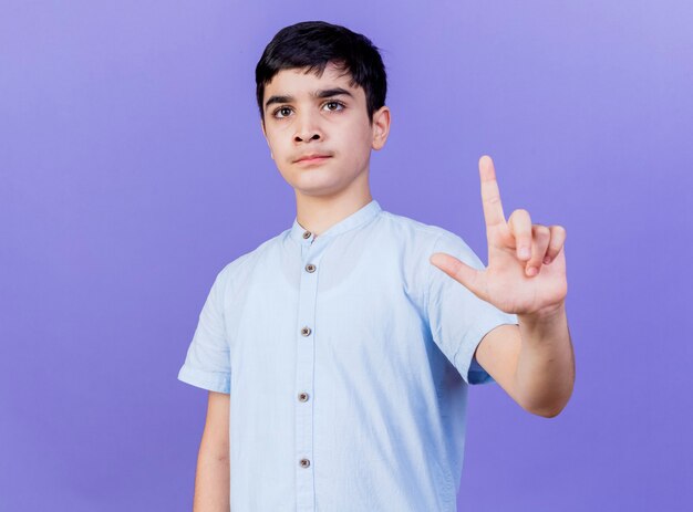 Jeune garçon strict à tout droit faisant le geste de perdant isolé sur mur violet