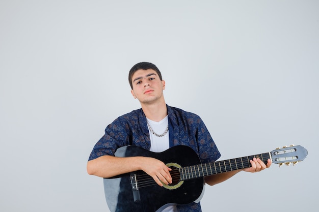 Jeune garçon en t-shirt jouant de la guitare alors qu'il était assis contre un homme et l'air confiant, vue de face.