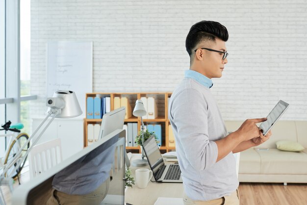 Jeune gestionnaire debout au bureau et en tapant sur le pavé tactile