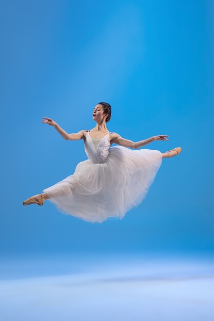 Jeune et gracieuse ballerine en robe blanche isolée sur mur bleu