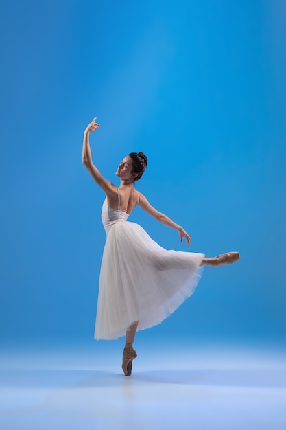 Photo gratuite jeune et gracieuse ballerine en robe blanche isolée sur mur bleu