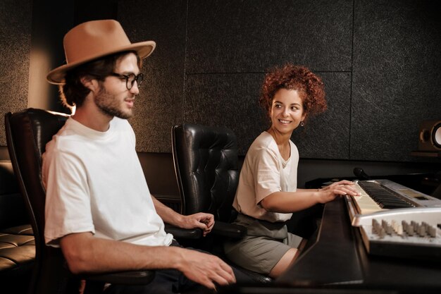 Jeune groupe de musique élégant composant une chanson sur un clavier de piano dans un studio d'enregistrement sonore moderne. Chanteurs attrayants travaillant ensemble sur un nouvel album de musique