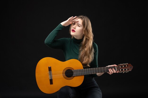 Jeune guitariste féminine concentrée tenant son instrument de musique préféré dans l'obscurité