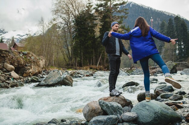 Jeune hipster beau couple amoureux marchant sur un rocher à la rivière dans la forêt d'hiver