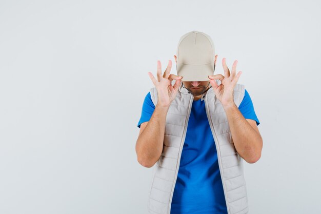 Jeune homme abaissant sa casquette sur les yeux en t-shirt, veste et à la cool, vue de face.