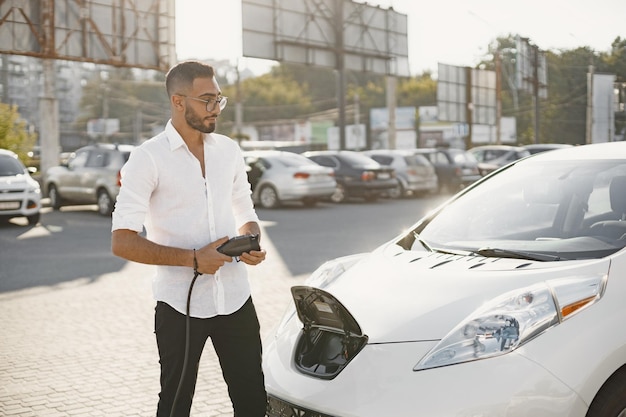 Jeune homme adulte chargeant sa voiture électrique dans la ville. Concept de voiture électrique écologique.