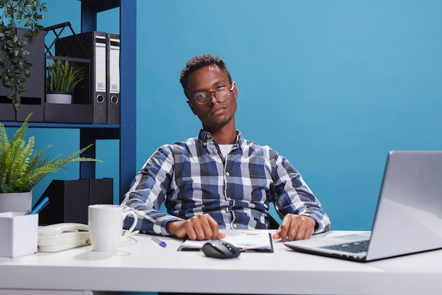 Jeune homme d'affaires adulte ennuyé et fatigué assis au bureau tout en regardant la caméra. Employé d'agence épuisé et fatigué avec une expression de visage d'ennui assis à l'intérieur de l'espace de travail.