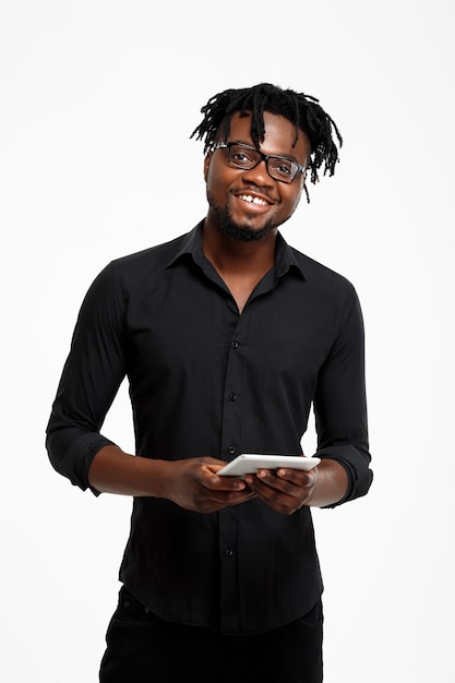 Jeune homme d'affaires africain prospère tenant la tablette, souriant sur blanc.